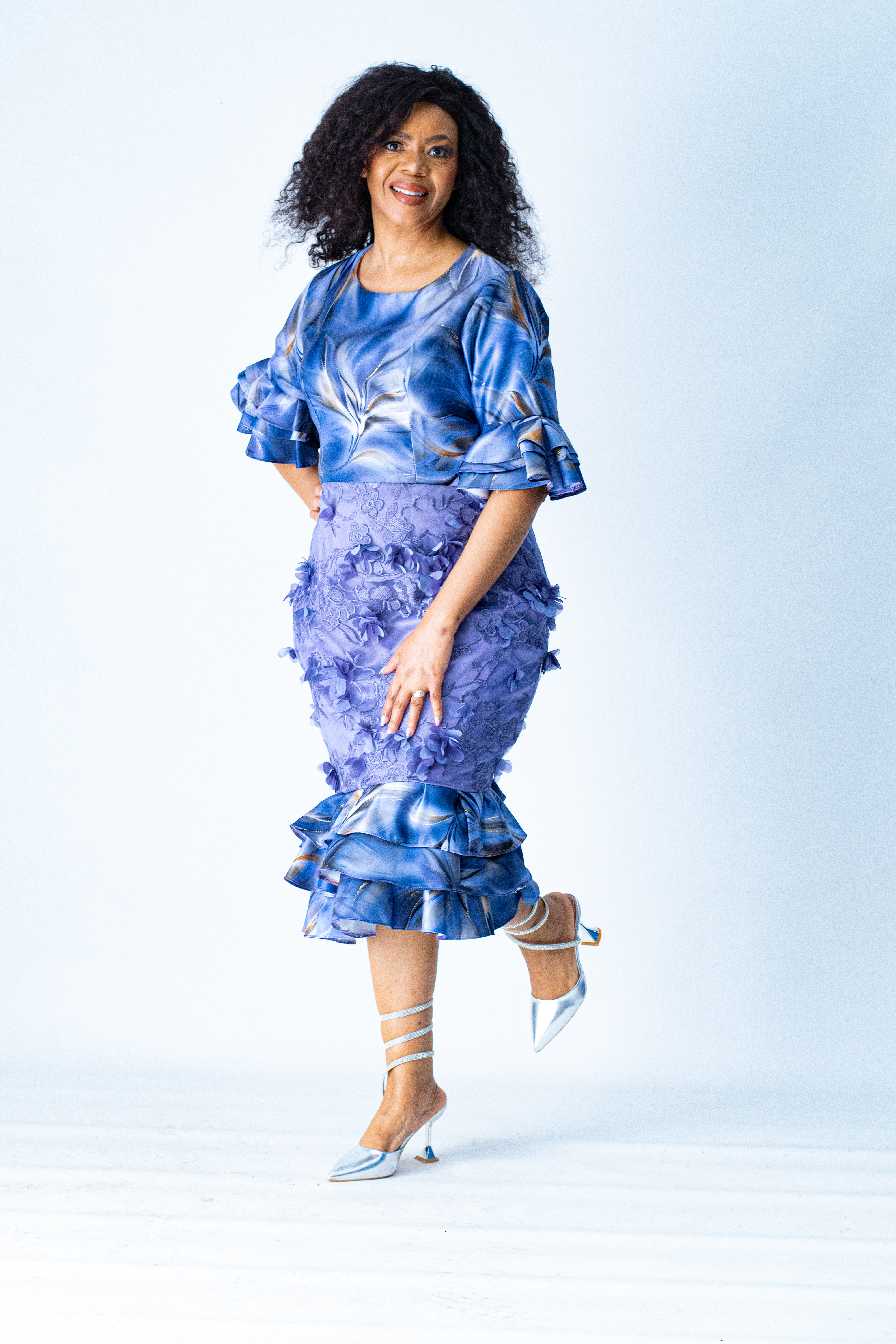 Smiling woman in a blue and purple dress posing against a white studio backdrop