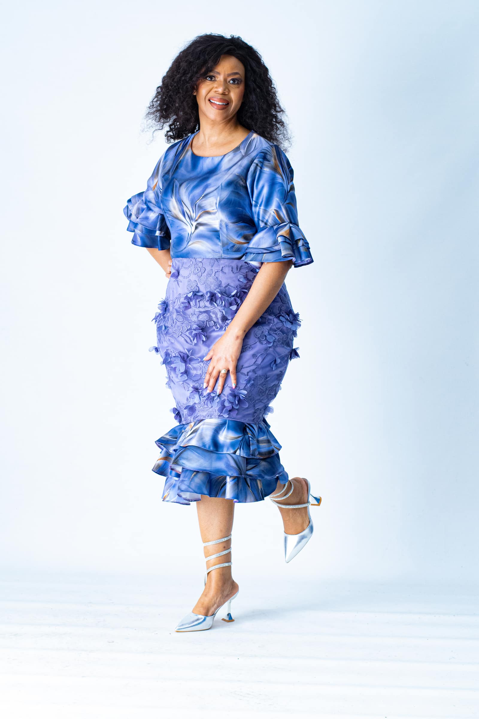 Smiling woman in a blue and purple dress posing against a white studio backdrop